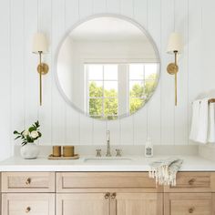 a bathroom with white walls and wooden cabinetry has a round mirror above the sink