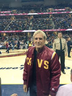 an older man wearing a maroon jacket and black tie standing in front of a crowd