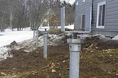 two metal poles are in the dirt near a house with snow on the ground and trees behind them