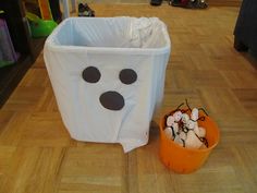 a white trash can sitting on top of a wooden floor next to a halloween decoration