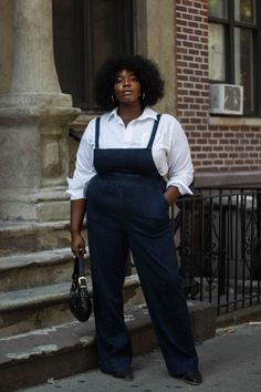 a woman standing on the sidewalk in front of a brick building with an afro hairstyle