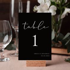 the table numbers are displayed on top of wooden blocks and place cards in front of wine glasses