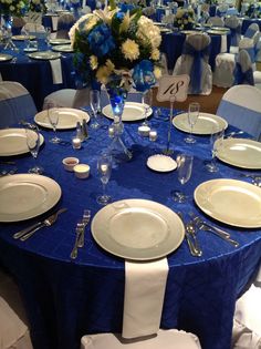 a blue table cloth with white plates and silverware is set for a formal function