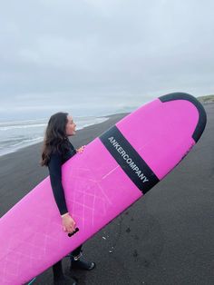 a woman holding a pink surfboard on the beach