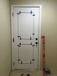 a white door with blue tape taped to it and some tools on the floor next to it