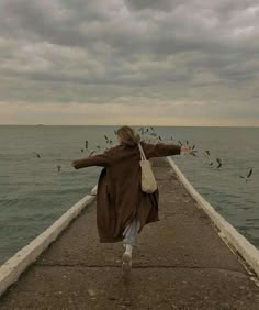 a woman is standing on the edge of a pier with seagulls in the background