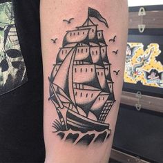 a black and white photo of a ship tattoo on the left arm with seagulls flying around it