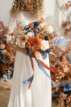 a woman in a white dress holding a bouquet of blue, orange and pink flowers