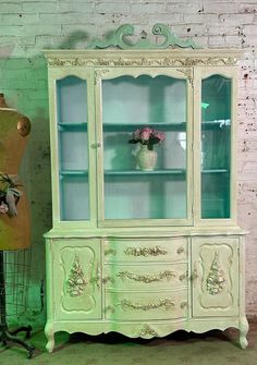 an antique china cabinet with flowers in vases on top and green lighting above it