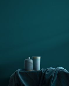 two vases sitting on top of a table covered in a blue cloth next to each other