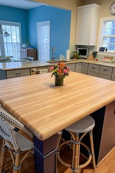 Kitchen Island with Hickory Butcher Block Countertop, flower centerpiece, cloth bar stools, grey cabinets, hardwood flooring.