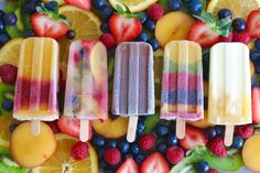 four popsicles are lined up with fruit on the top one is blueberries, oranges and raspberries