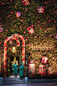 two people are standing in front of a christmas tree with lights and decorations on it