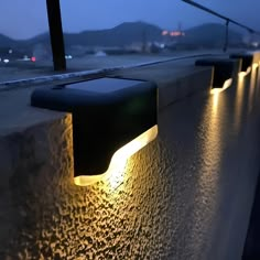 some lights that are sitting on the side of a building near water and mountains in the background