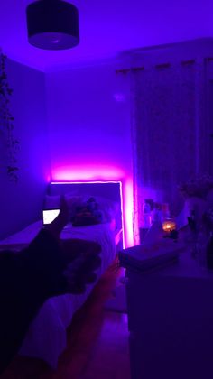 a person sitting in a room with purple lights on the walls and bed, next to a window