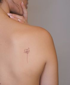 a woman's back with a small tattoo on her left shoulder and a single flower in the middle