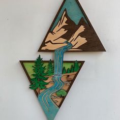 a triangle shaped wall hanging with a river and mountains in the center, on top of a white wall