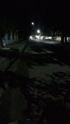 a dark street at night with cars parked on the side and trees in the foreground