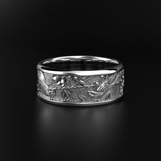 a wedding band with birds and flowers engraved on the side in white gold, sitting on a black surface