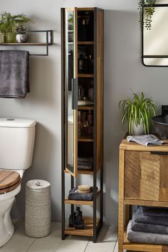 a bathroom with a wooden cabinet next to a white toilet and a potted plant