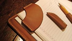 a leather wallet sitting on top of a wooden table next to a pen and paper