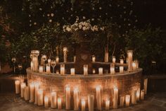 many lit candles are arranged in a circular arrangement on a stone platform surrounded by greenery