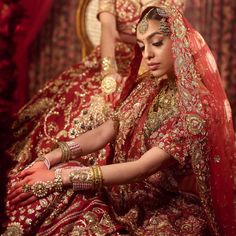 a woman in a red and gold bridal gown sits on a chair with her hands clasped