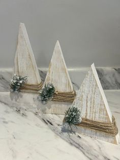 three white wooden christmas trees on a marble counter top with pine cones and evergreen needles