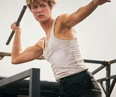 a young man holding a baseball bat on top of a metal structure in front of a white sky