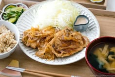 a white plate topped with food next to bowls of rice and chopsticks