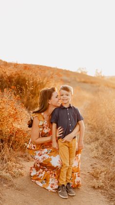 a mother and son hugging each other on a dirt path in the middle of a field