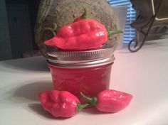 three red peppers sitting on top of a table next to a jar