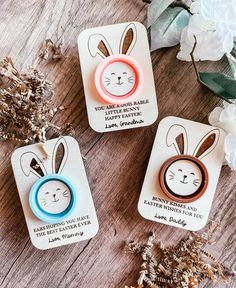 three easter bunny magnets on top of a wooden table with flowers and greenery