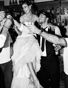 a woman in a white dress is being lifted into the air by two men at a bar