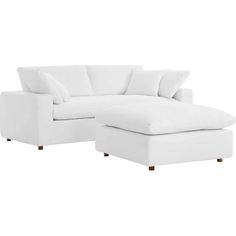 a white sectional couch with pillows on it and a footstool in the middle