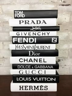 a stack of black and white books sitting on top of a wooden table next to a brick wall