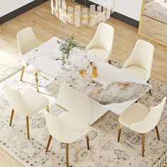 a dining room table with white chairs and a rug on the floor in front of it