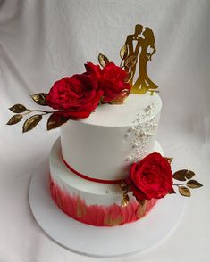 a wedding cake decorated with red roses and gold leaves on white tablecloths,