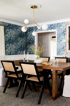 a dining room with blue wallpaper and wooden table surrounded by wicker chairs in the center