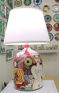 a lamp that is sitting on top of a white table next to a wall covered with pictures