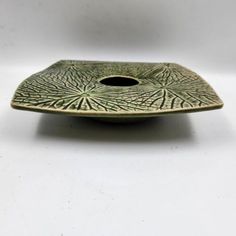 a small green bowl with a hole in the center on a white surface, it appears to be holding something