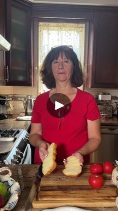 a woman in a red shirt is cutting bread on a wooden board with tomatoes and peppers