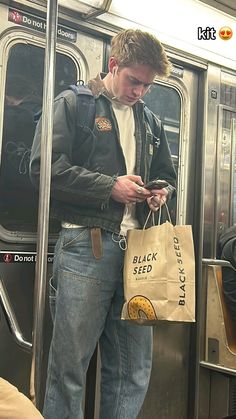 a young man standing on a subway looking at his cell phone while holding a bag