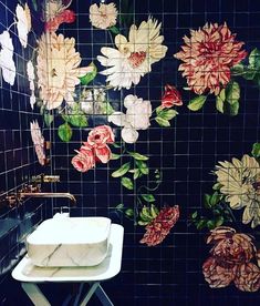 a black tiled bathroom with flowers on the wall and sink in front of it's mirror