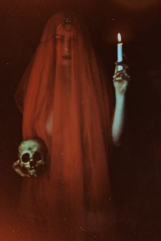 a woman holding a lit candle in her hand with a skull on the other side