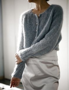 a woman wearing a gray sweater and white skirt