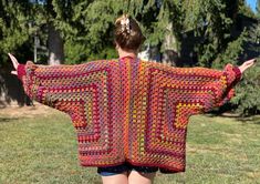 a woman wearing a colorful crocheted granny shawl in the grass with her arms outstretched