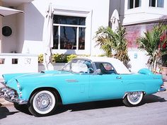 an old blue car is parked in front of a white building with palm trees on the sidewalk