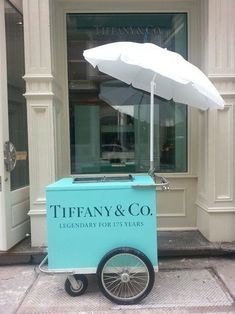 an ice cream cart on the sidewalk with an umbrella in front of a storefront