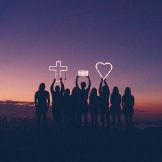 silhouettes of people holding up crosses and hearts at sunset with the sun setting in the background